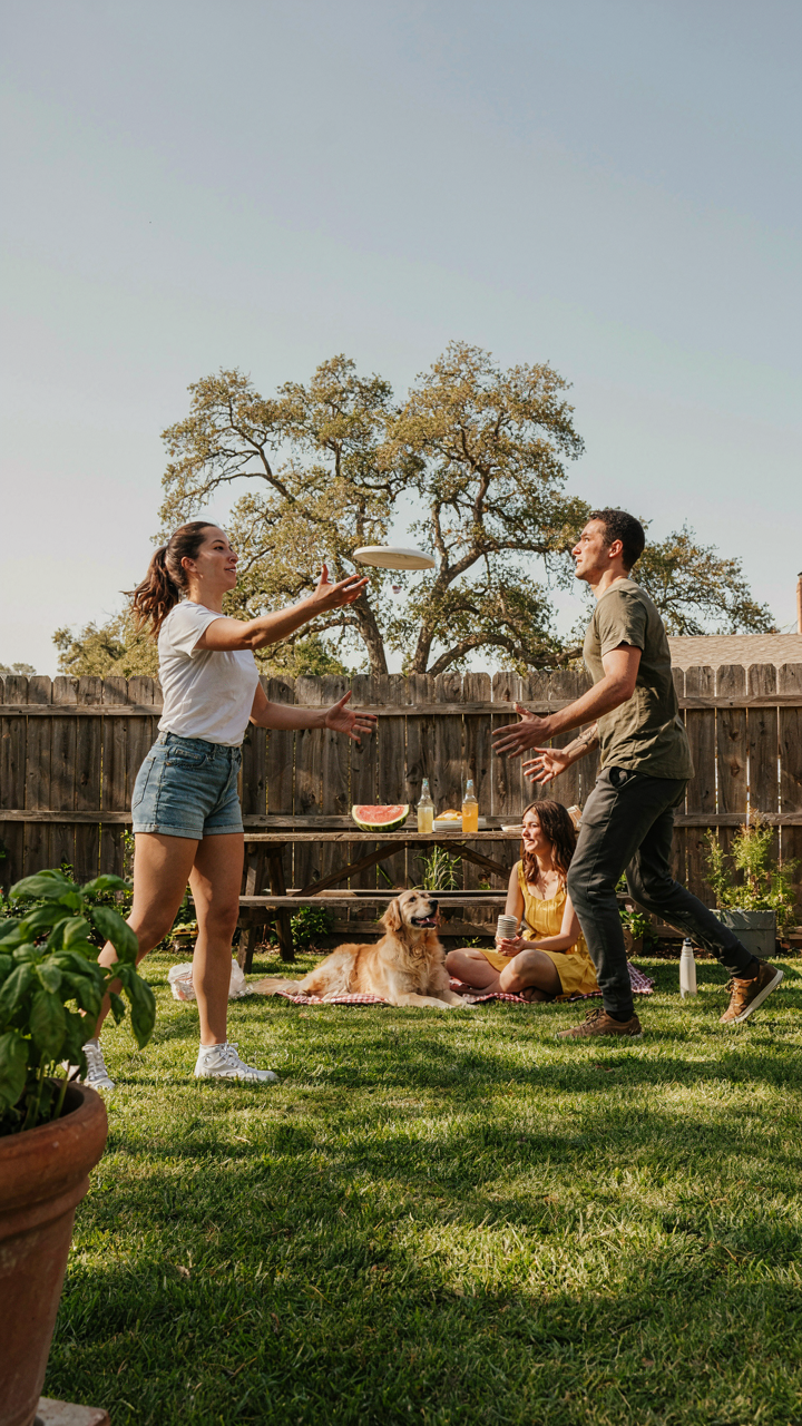 Guests casually toss a frisbee in a sunny backyard.