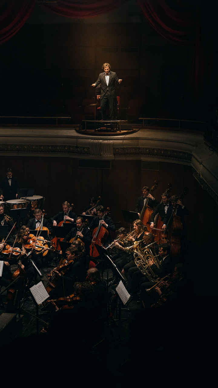 A conductor leads an orchestra in a concert hall with instruments arranged perfectly.