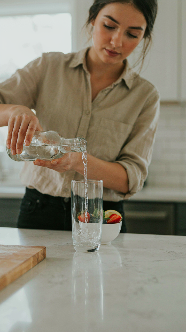 A person pours sparkling water into a glass, with fruit nearby.