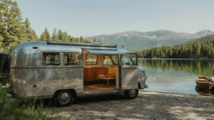 A refurbished aluminum camper remodel sits by a lake, showing its mid-century modern interior.