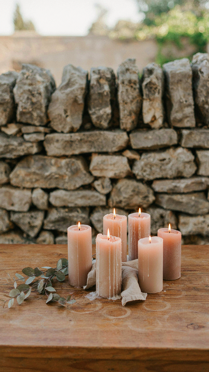 A miniature stone wall protects lit pillar candles on an outdoor table.