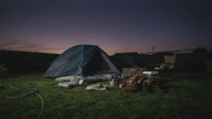 A messy backyard campout setup at dusk with a tent and gear.