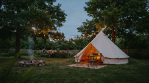 An elegant glamping tent glowing at dusk in a lush backyard, string lights draped above.