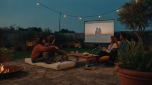 Friends gather on comfortable outdoor seats to watch a backyard movie night.
