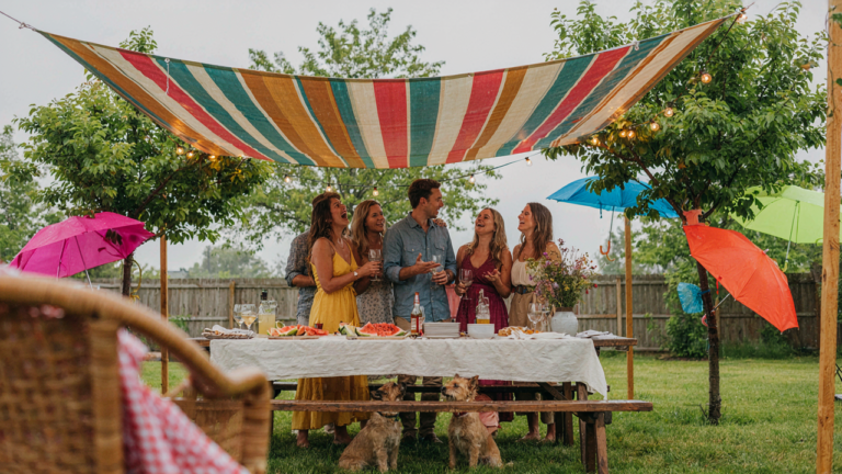 A festive backyard party continues under a large canopy during a light rain shower.