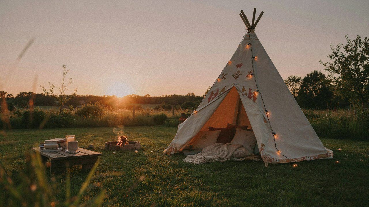 A charming backyard teepee tent lit with string lights at dusk, ready for a sleepover.