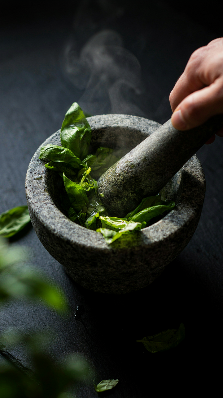 A mortar and pestle muddle fresh green basil leaves, releasing their aroma.