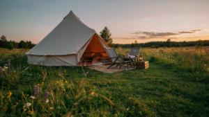 A comfortable bell tent setup glowing warmly in a meadow at sunset.