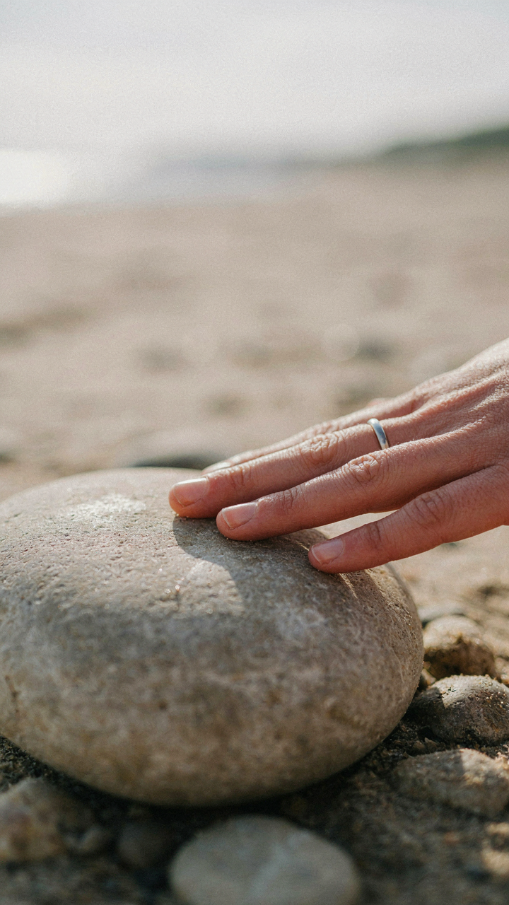 A hand touches a warm, smooth rock heated by the sun.