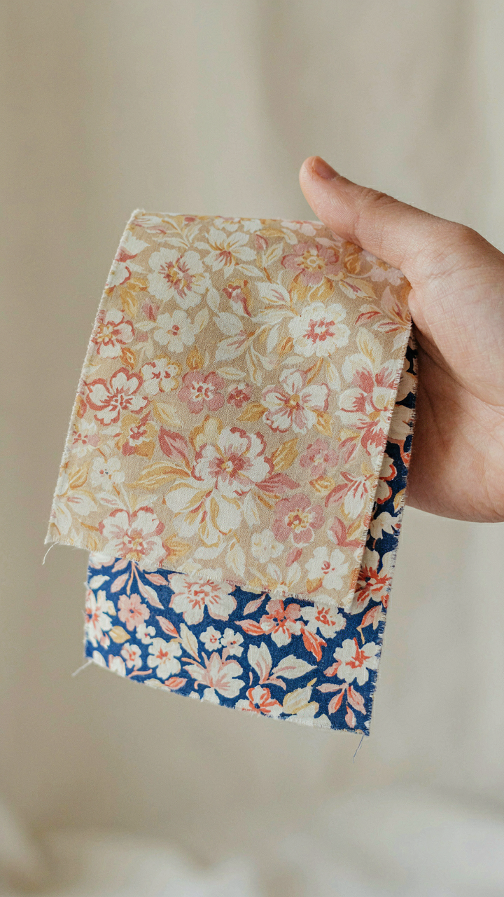A hand holds up old faded fabric next to new, colorful fabric.