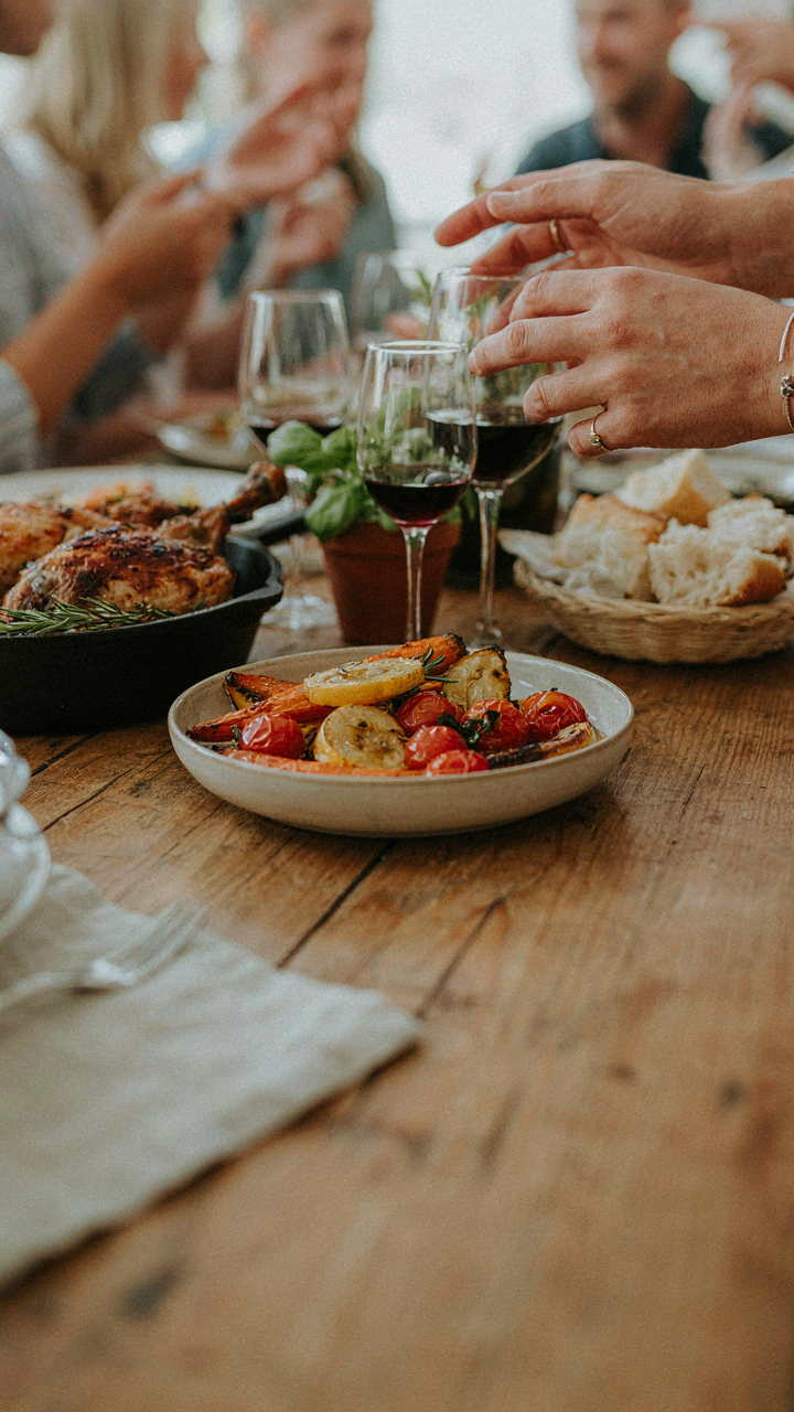 Many hands reach for colorful family style outdoor dinner dishes on a rustic table.