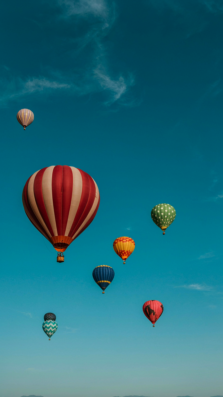 Hot air balloons float through a clear blue sky.