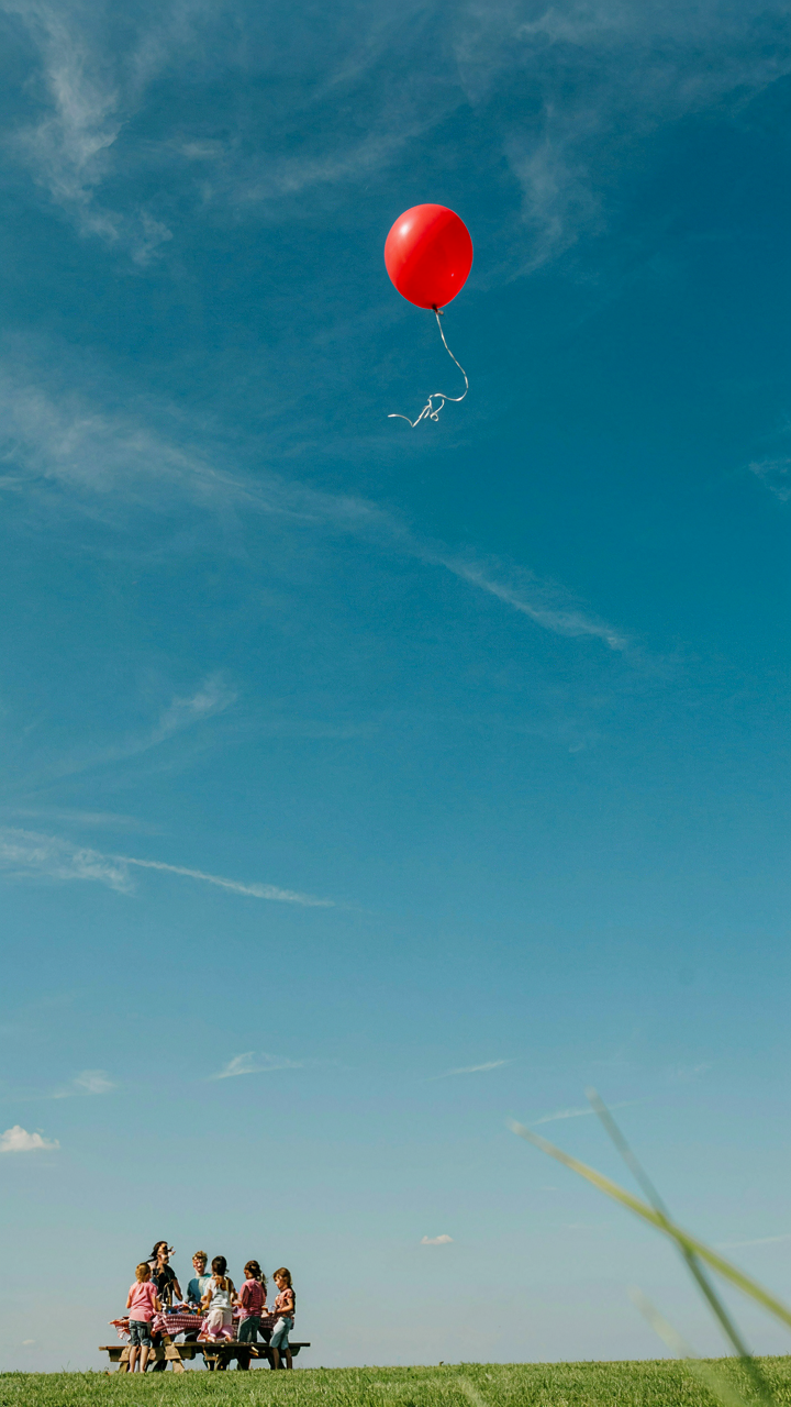 One colorful balloon floats high in the bright blue sky, leaving a party.