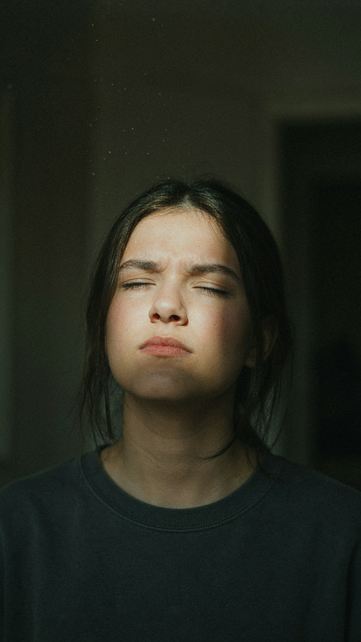 A person squints under a bright spotlight in a dark room.