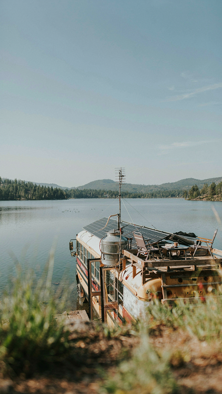A skoolie rooftop has solar panels, a water tank, and a small deck.