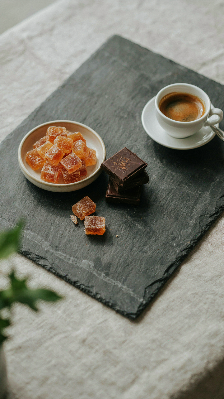 Candied ginger and dark chocolate squares next to an espresso cup.
