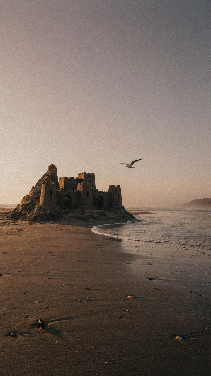 A crumbling sandcastle on a beach as waves wash over it.