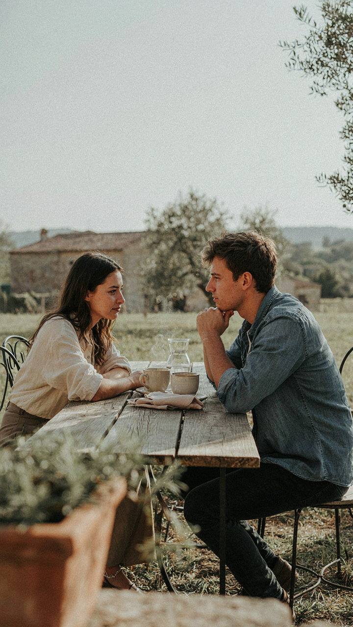 Two friends talk closely at a rustic outdoor table setting.