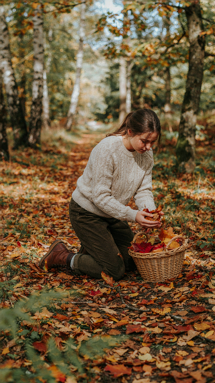 A person gathers colorful fallen leaves, acorns, and small branches from a forest.