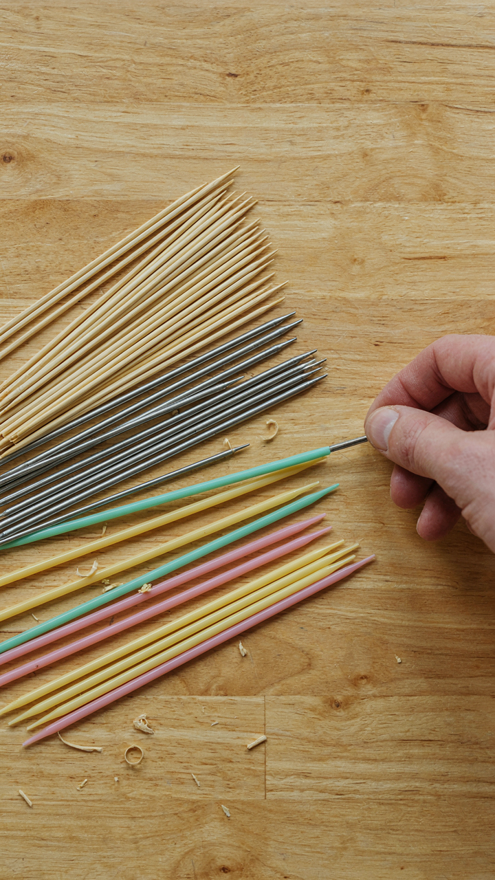 Bamboo, metal, and plastic skewers laid out on a wooden surface.