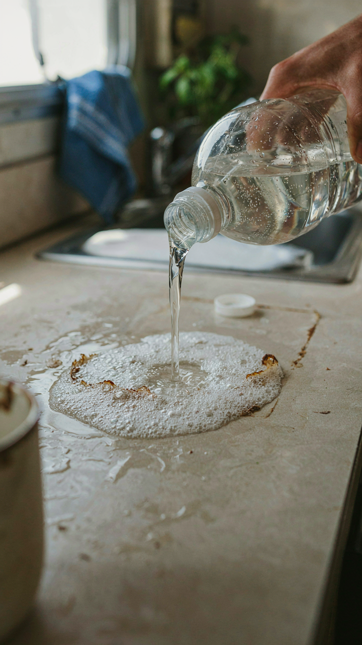 White vinegar being poured onto a dirty surface in an RV kitchen.