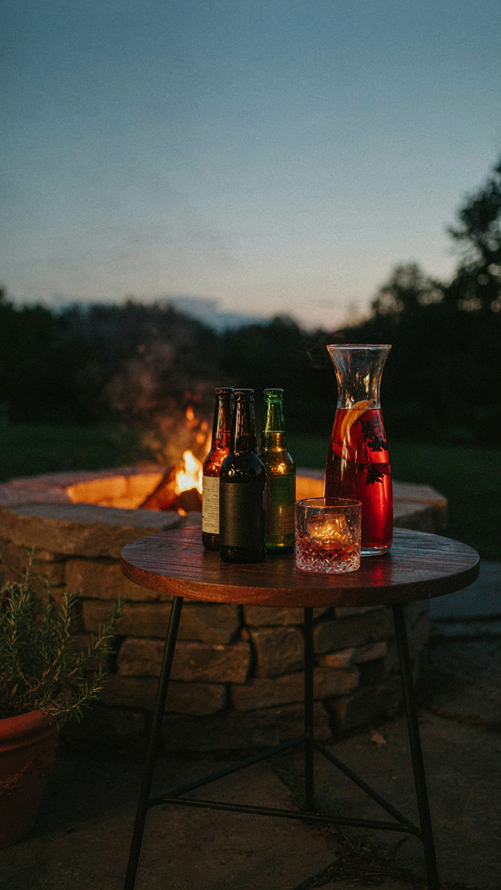 Sophisticated adult beverages are arranged on a table at a fire pit party.
