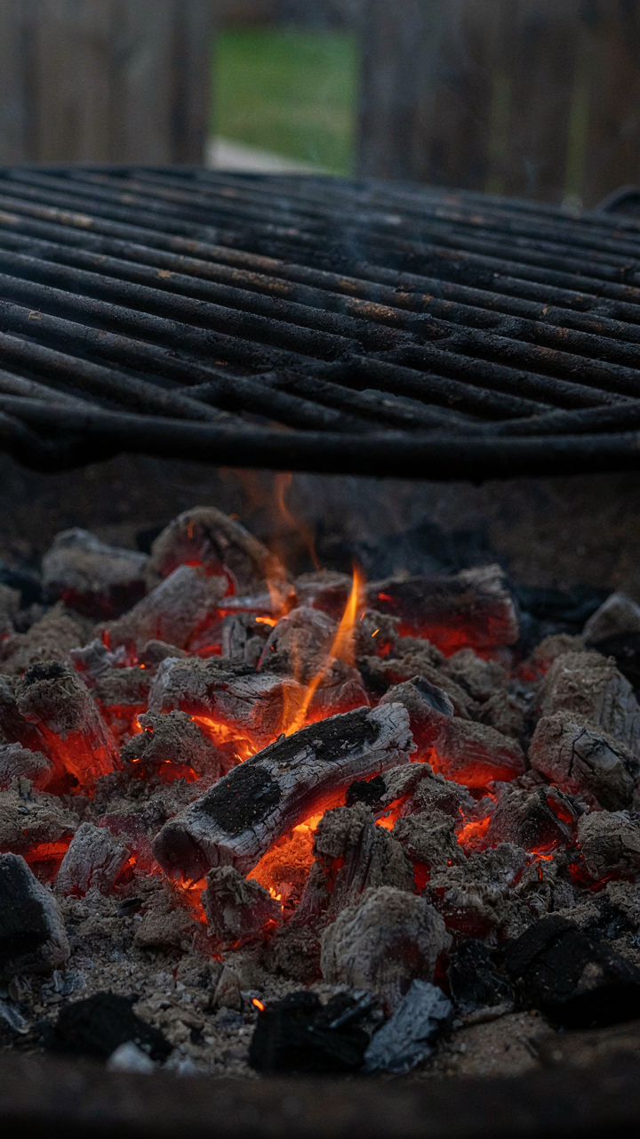 Glowing red charcoal briquettes in a fire pit, ready for cooking backyard campout food.