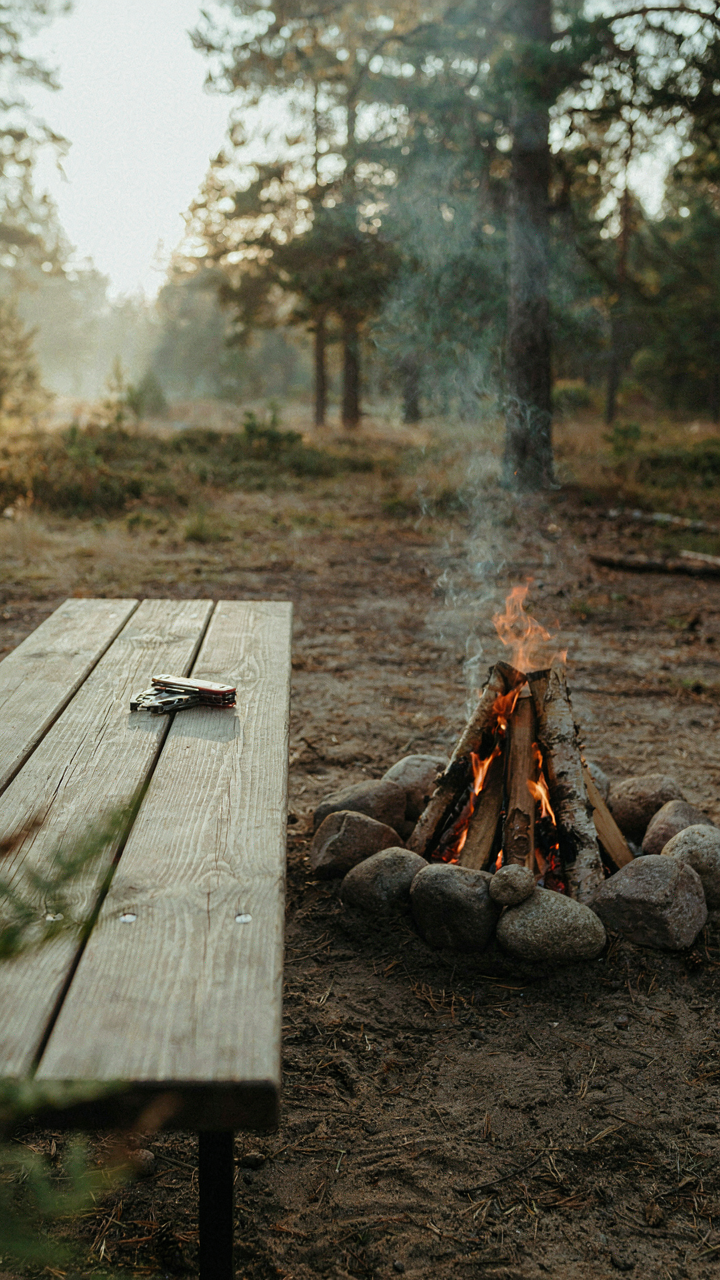 A multi-tool rests on a small table near a simple campfire.