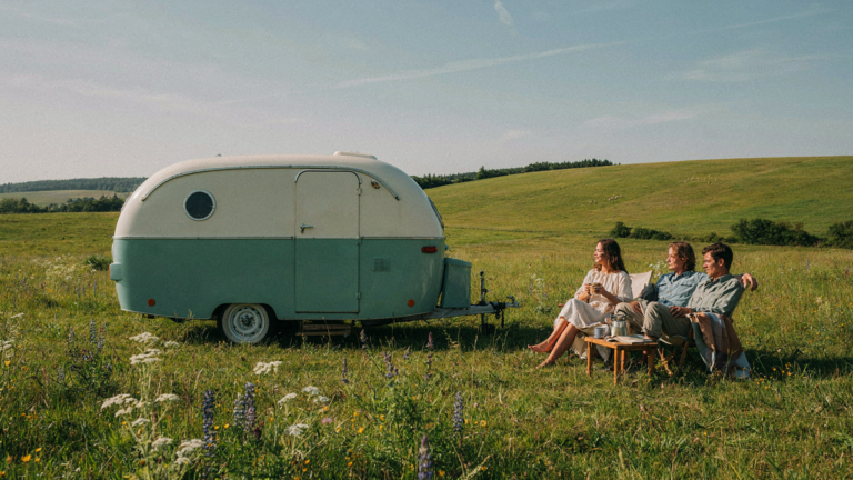 A restored vintage camper with fresh two-tone camper exterior paint sits in a sunny meadow.