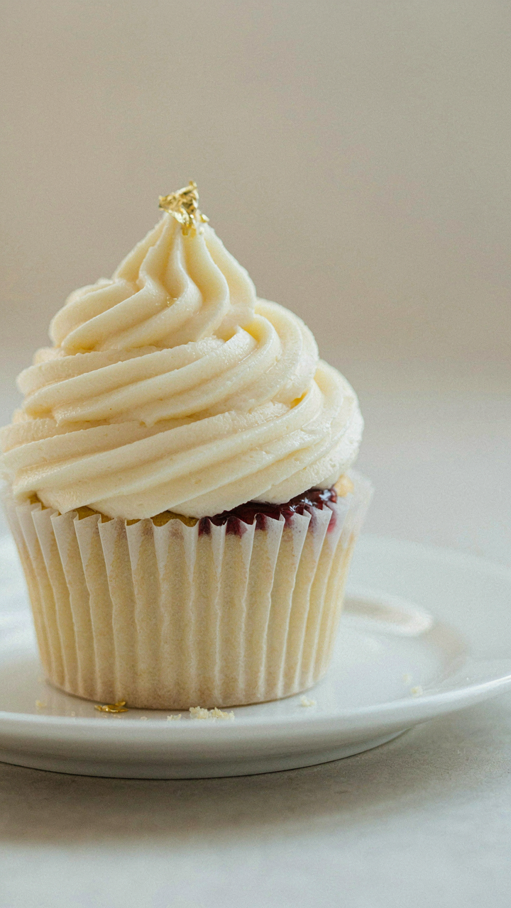 A detailed gourmet cupcake with fancy frosting sits on a white plate.