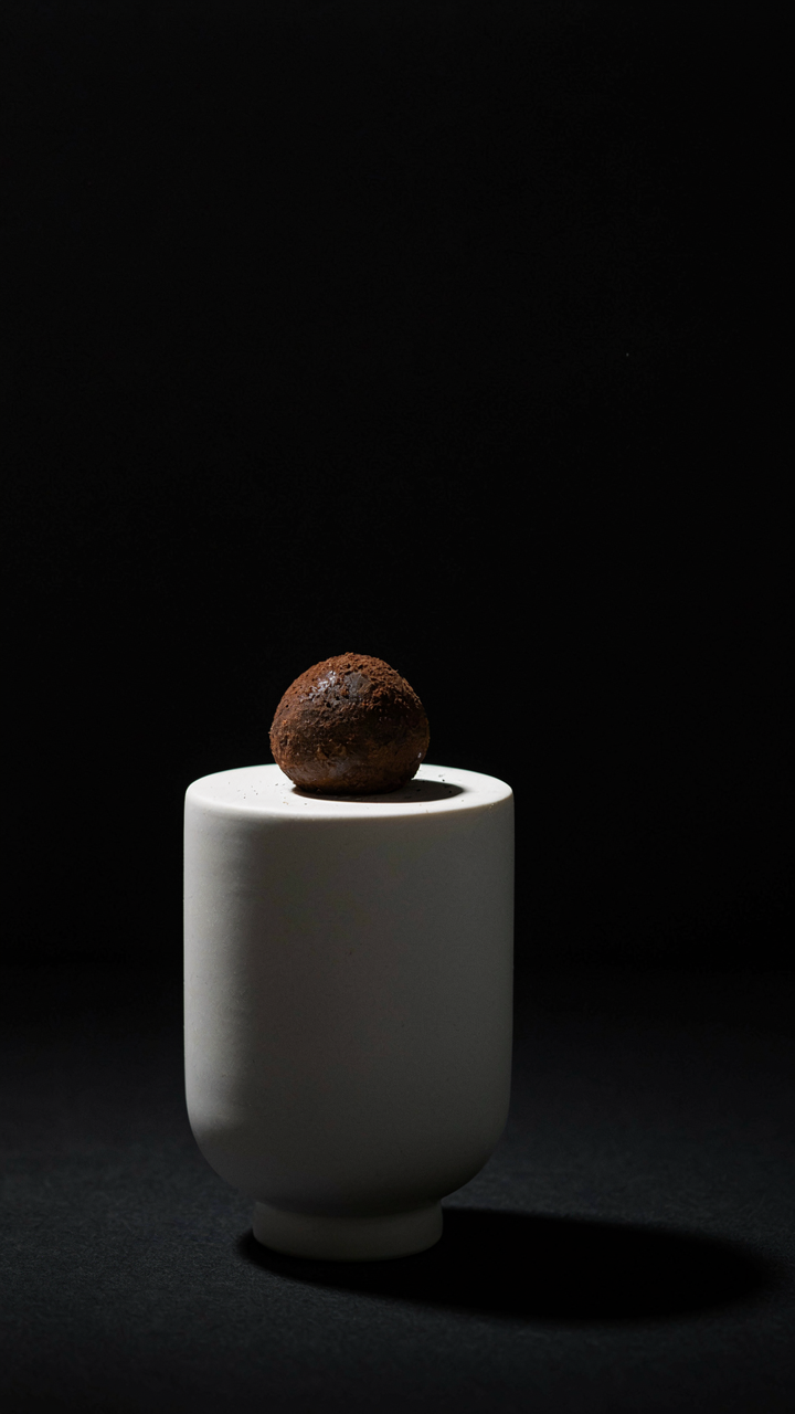 A single dark chocolate truffle on a white pedestal.