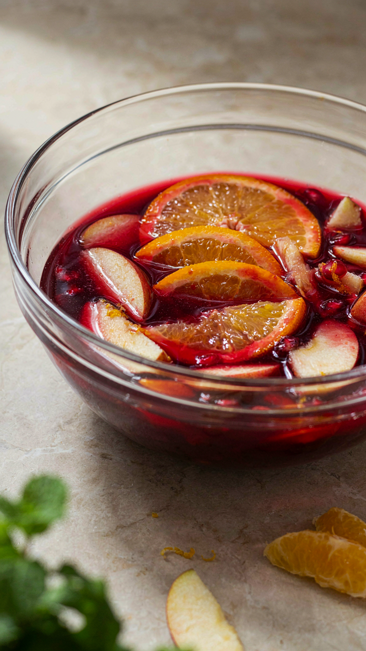 Sliced fruit soaking in a large glass bowl of red liquid.