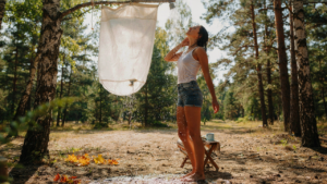 A person uses a simple diy camp shower in a sunny forest setting.