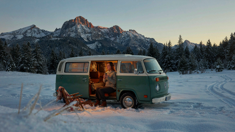 A warm, cozy camper van sits in a snowy mountain setting.