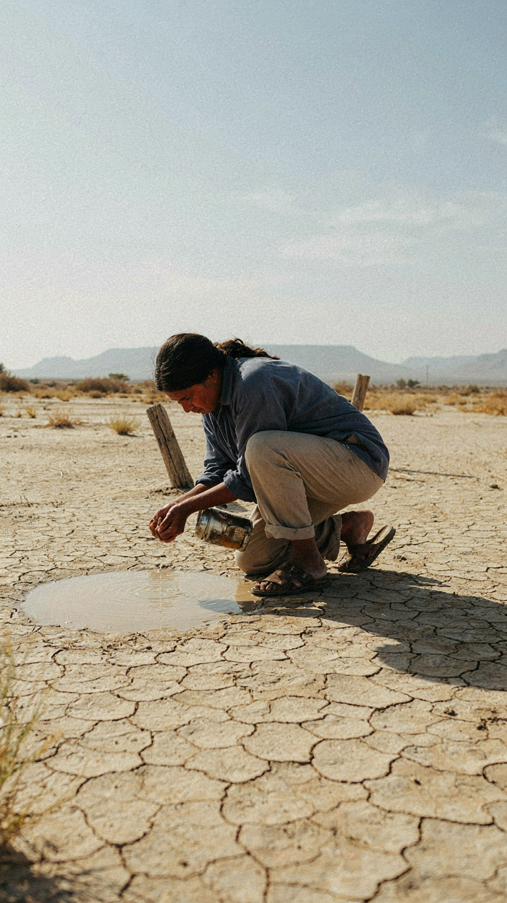 A person collects tiny drops of water in a vast, dry desert.