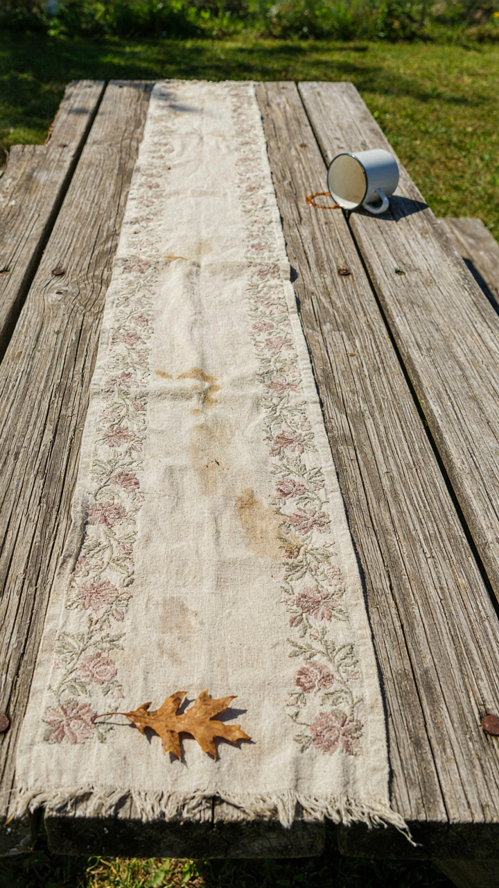 A faded and stained indoor table runner on an outdoor picnic table.