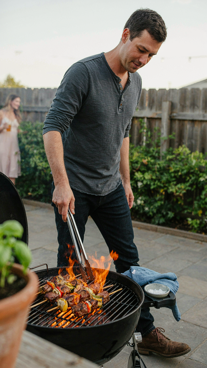 A person confidently tends a professional grill, expertly flipping skewers.