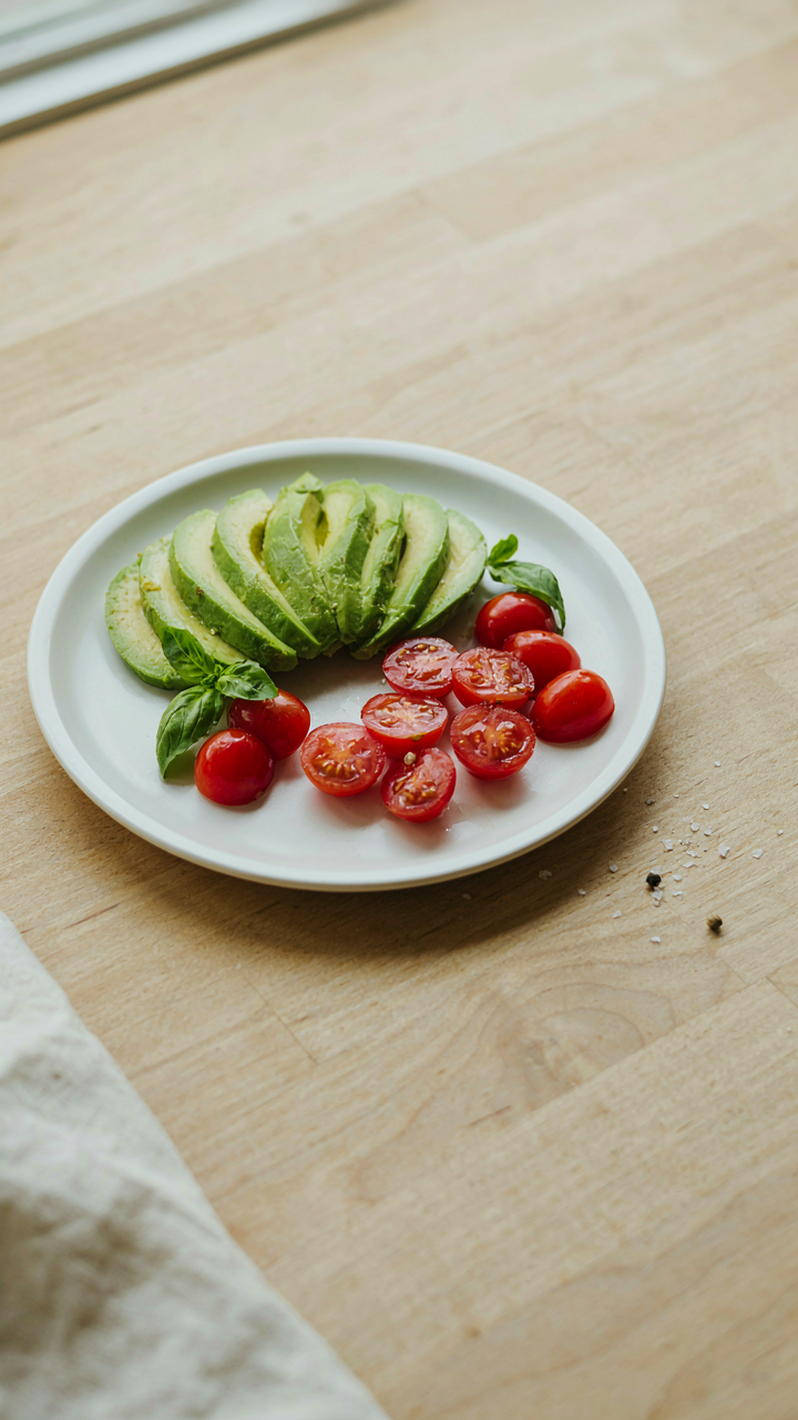A plate with contrasting green avocado and red cherry tomatoes.