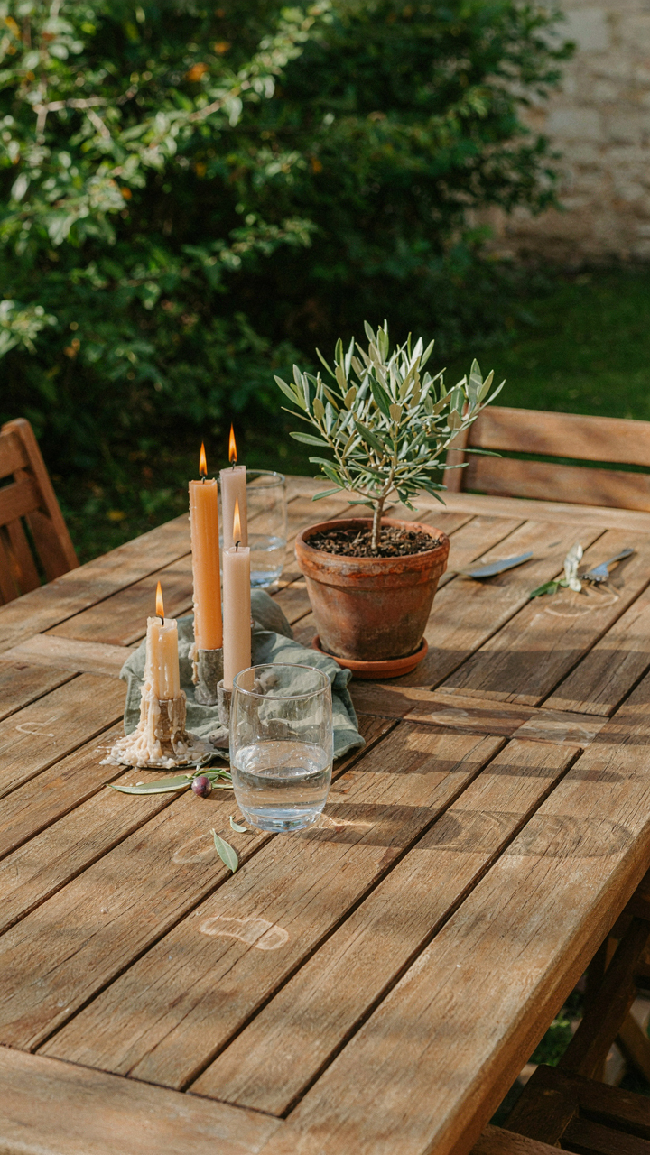 An outdoor dining table has an asymmetric arrangement of candles and a small plant.