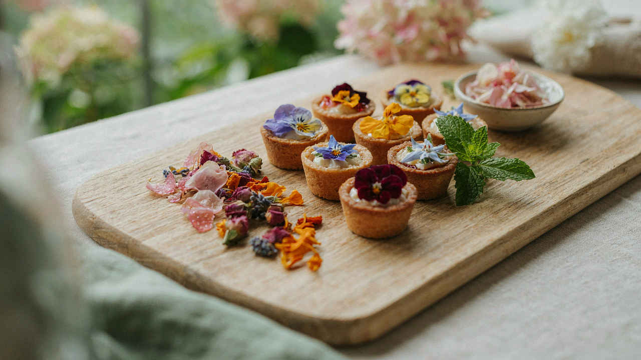 A beautiful assortment of colorful edible flower snacks on a rustic wooden board at a garden party.