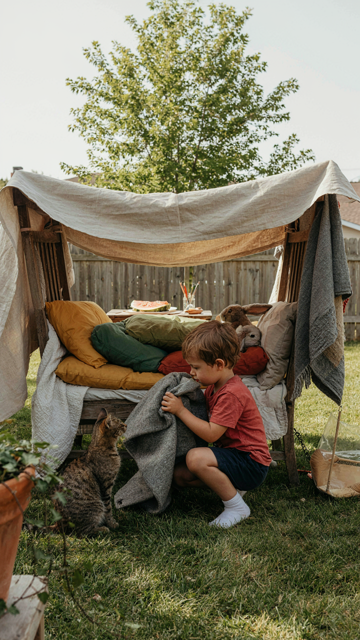 A child is very focused building a blanket fort in a backyard.