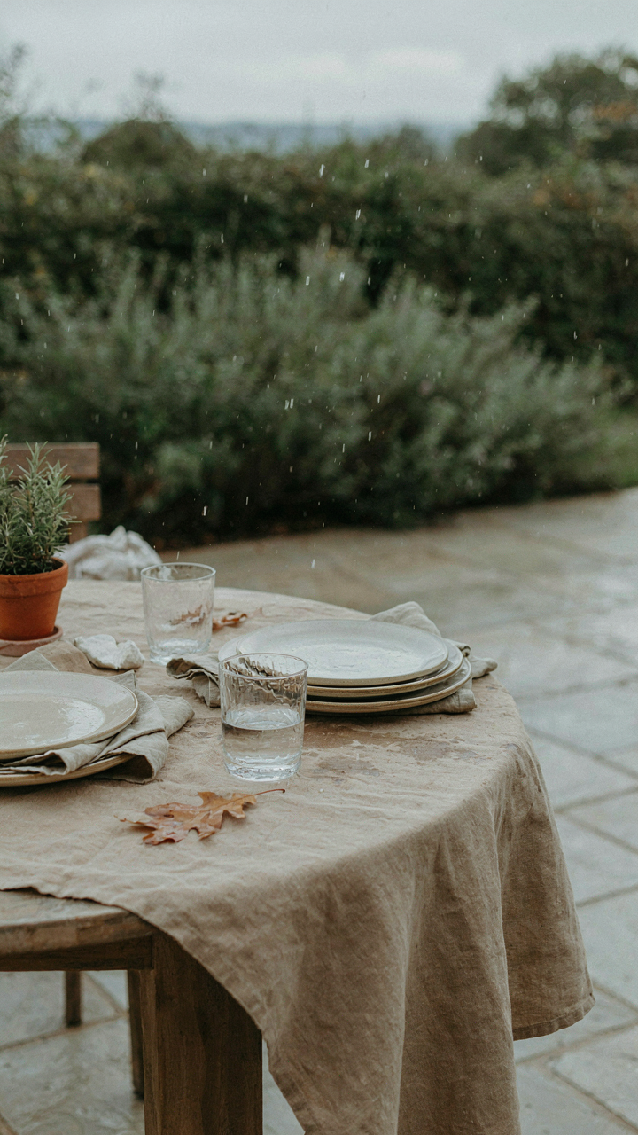 Durable canvas tablecloth and ceramic plates are on an outdoor table as rain starts.