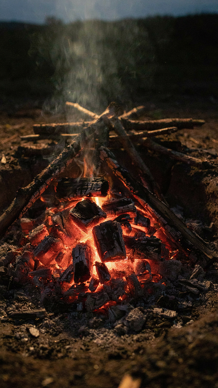 Red-hot hardwood coals glow in a campfire pit.