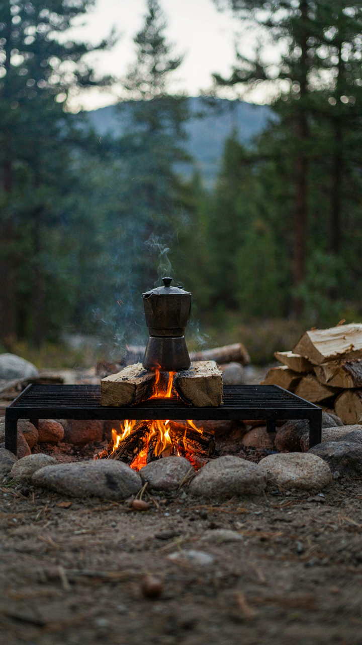 A metal percolator gently bubbles on a grate over a controlled campfire.