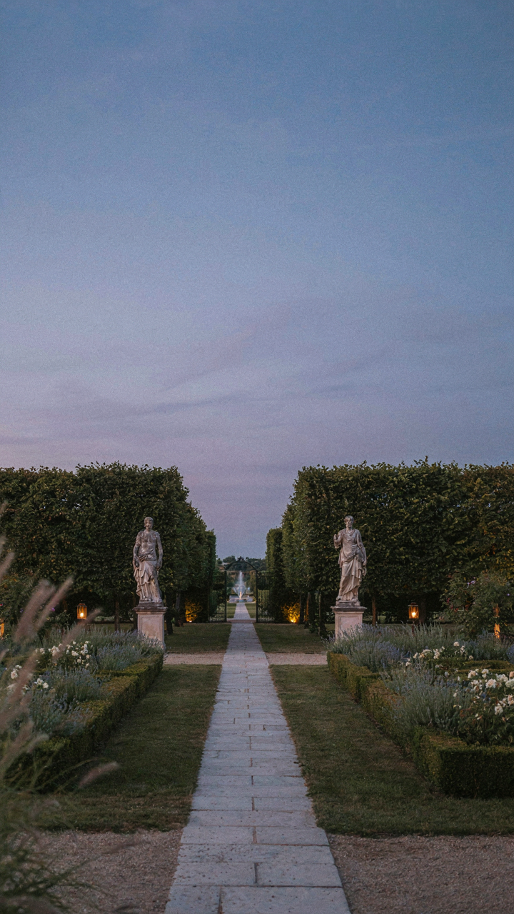 An elegant formal garden at dusk with subtle evening garden party lighting.