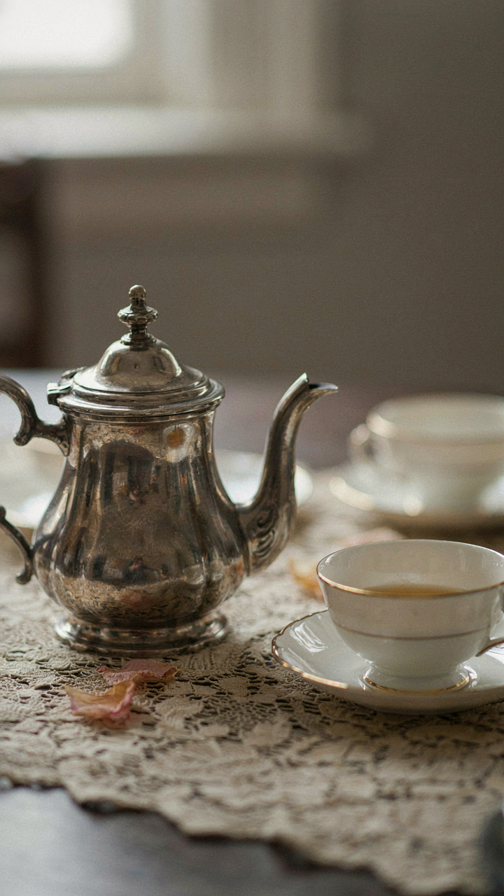 An antique silver teapot and teacup sit on a lace tablecloth.