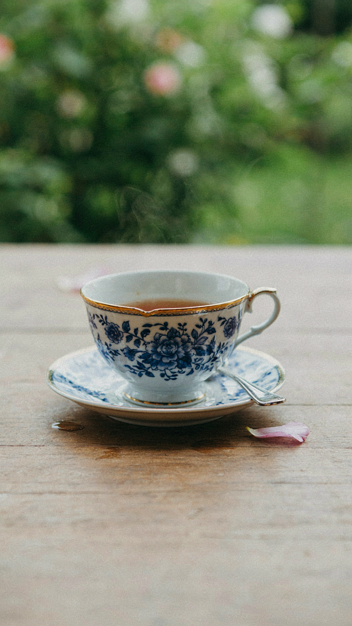 A single, ornate teacup on a plain wooden table at a garden tea party.