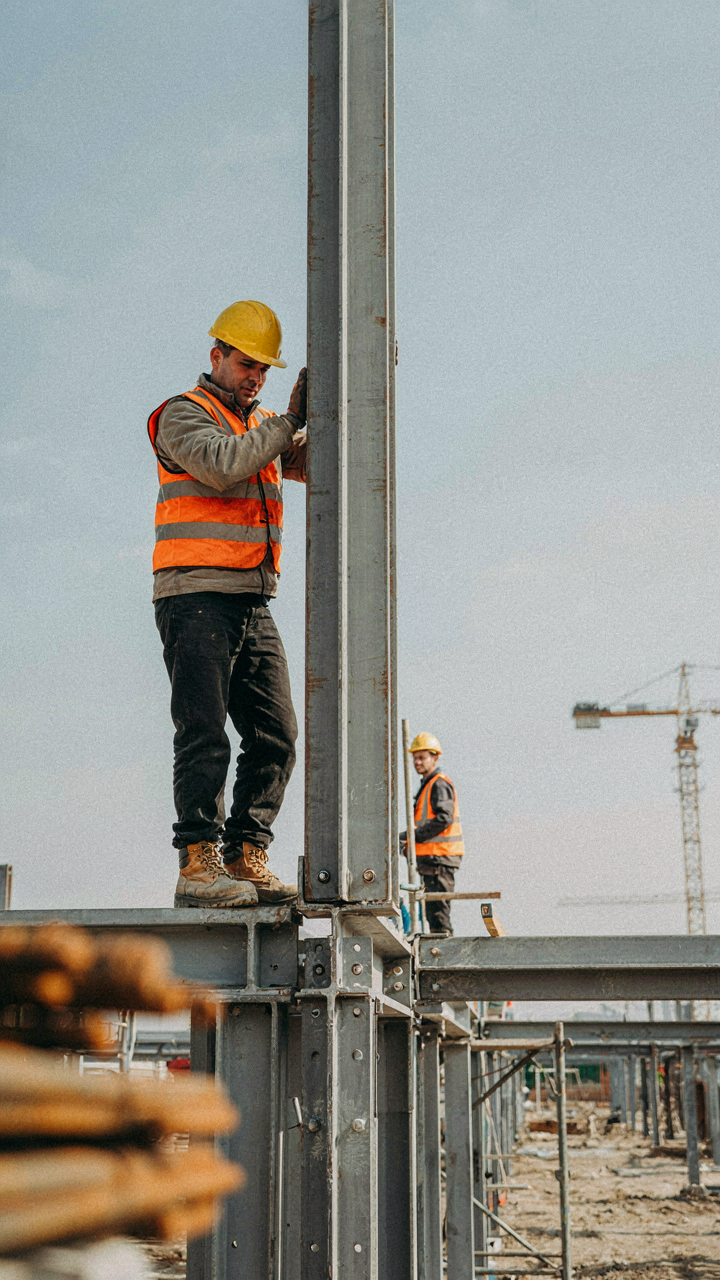 A construction worker balances a large steel beam on a frame.