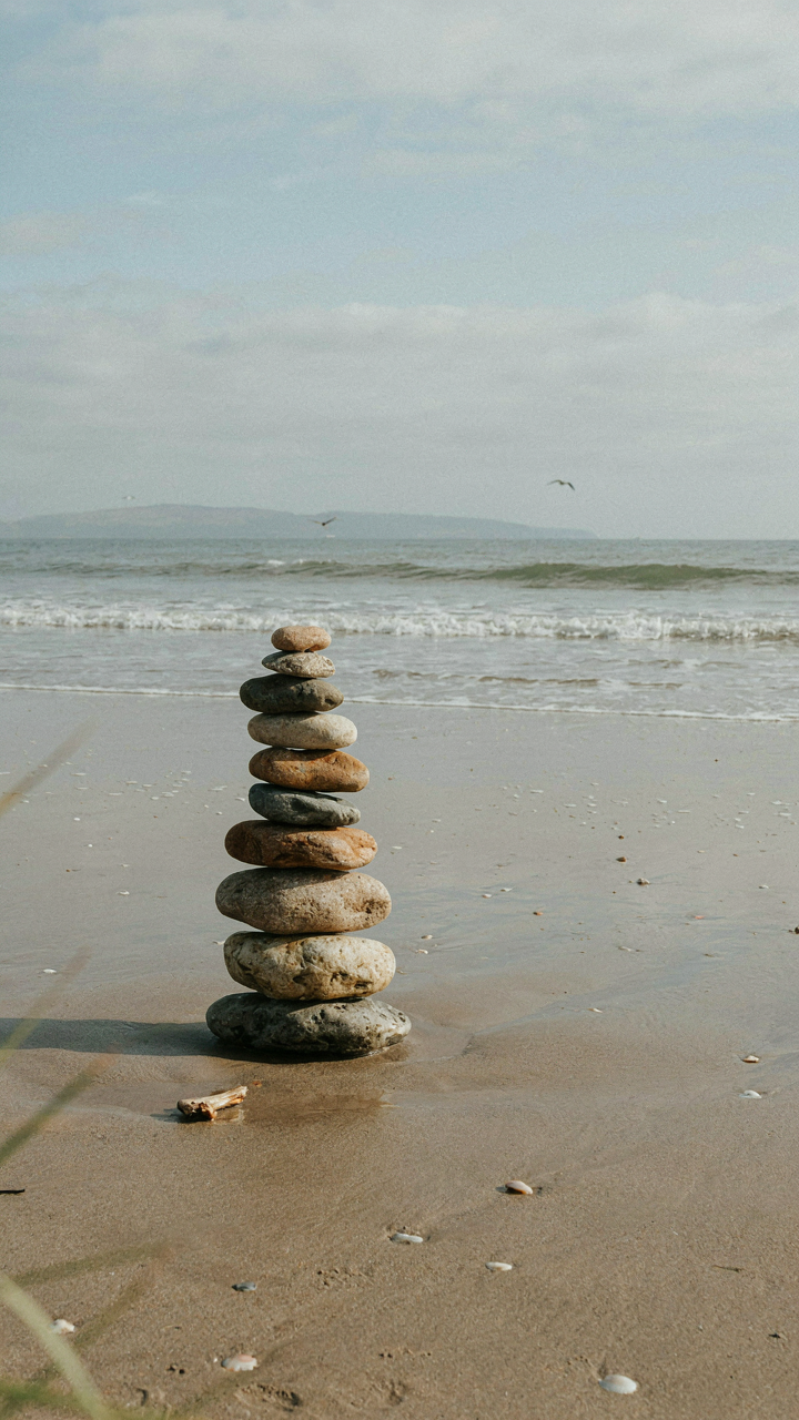 A stack of smooth, heavy stones is perfectly balanced on a beach near gentle waves.