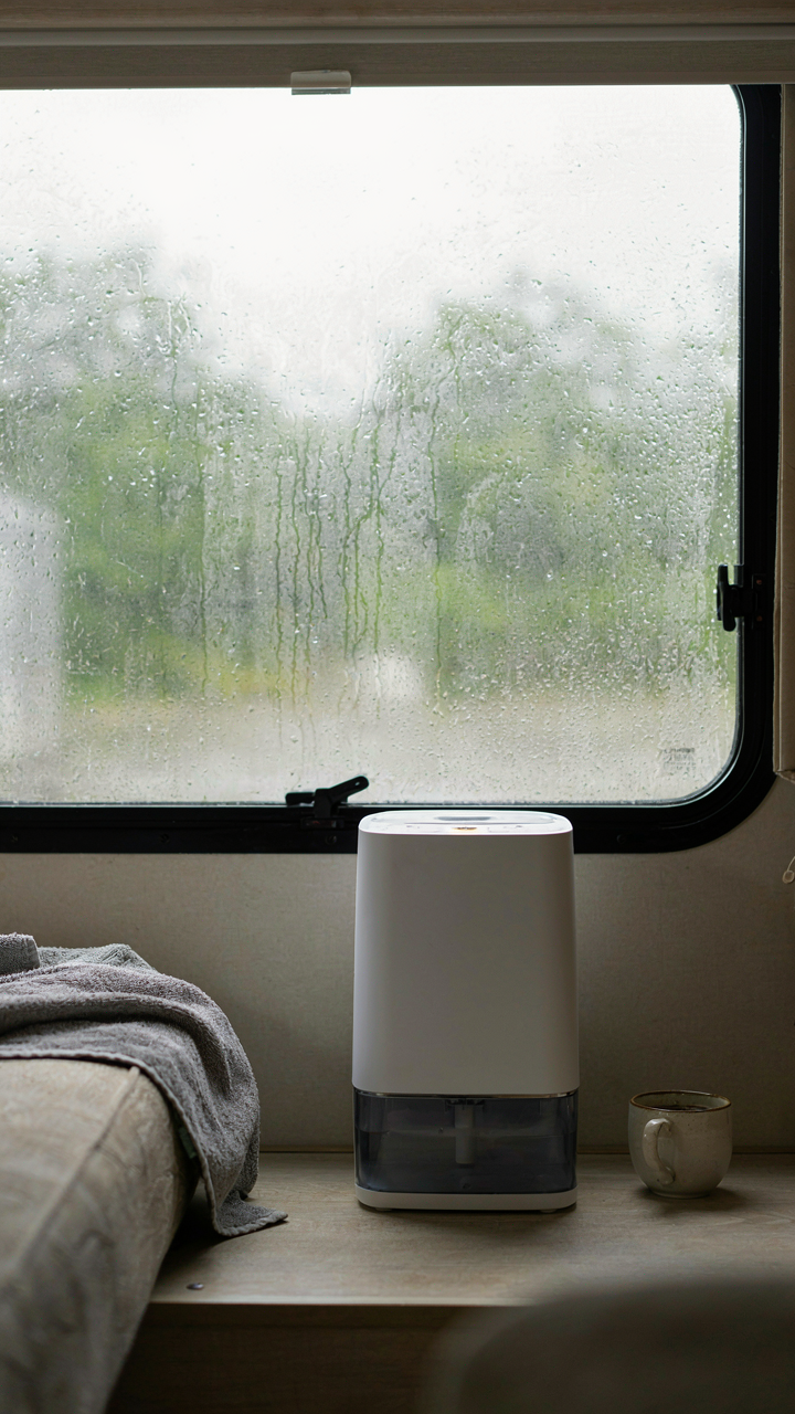 Condensation drips down an RV window, a small dehumidifier nearby.